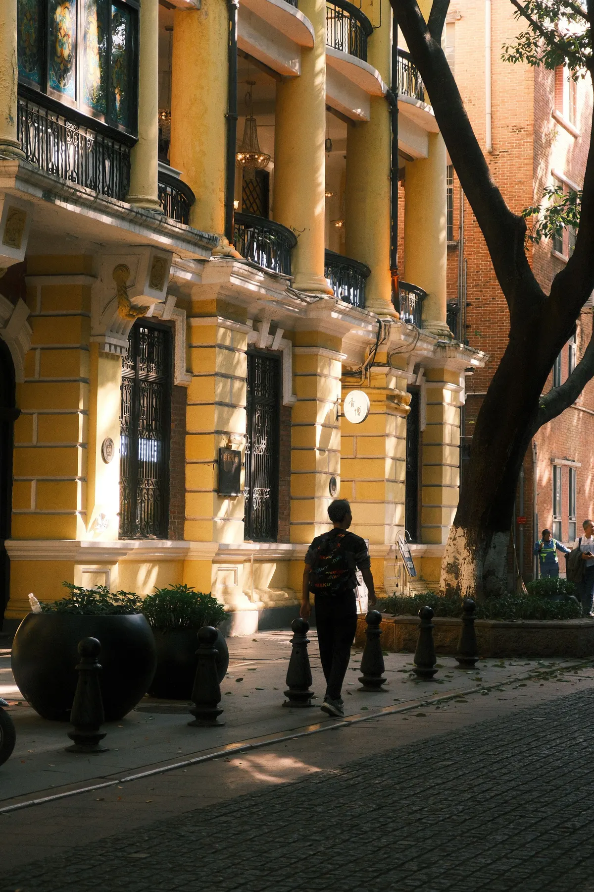 Sunlit colonial arcade buildings and plane trees on a quiet Shamian Island street in Guangzhou