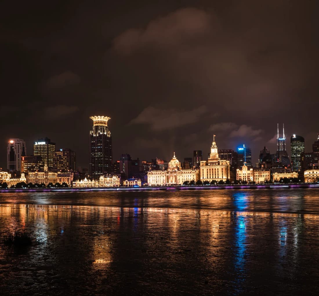 The Bund waterfront in Shanghai at night, historic buildings lit in gold along the Huangpu River
